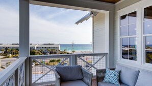 Ein Balkon mit Blick auf den Strand und das Meer, ein graues Sofa und ein Korbstuhl.