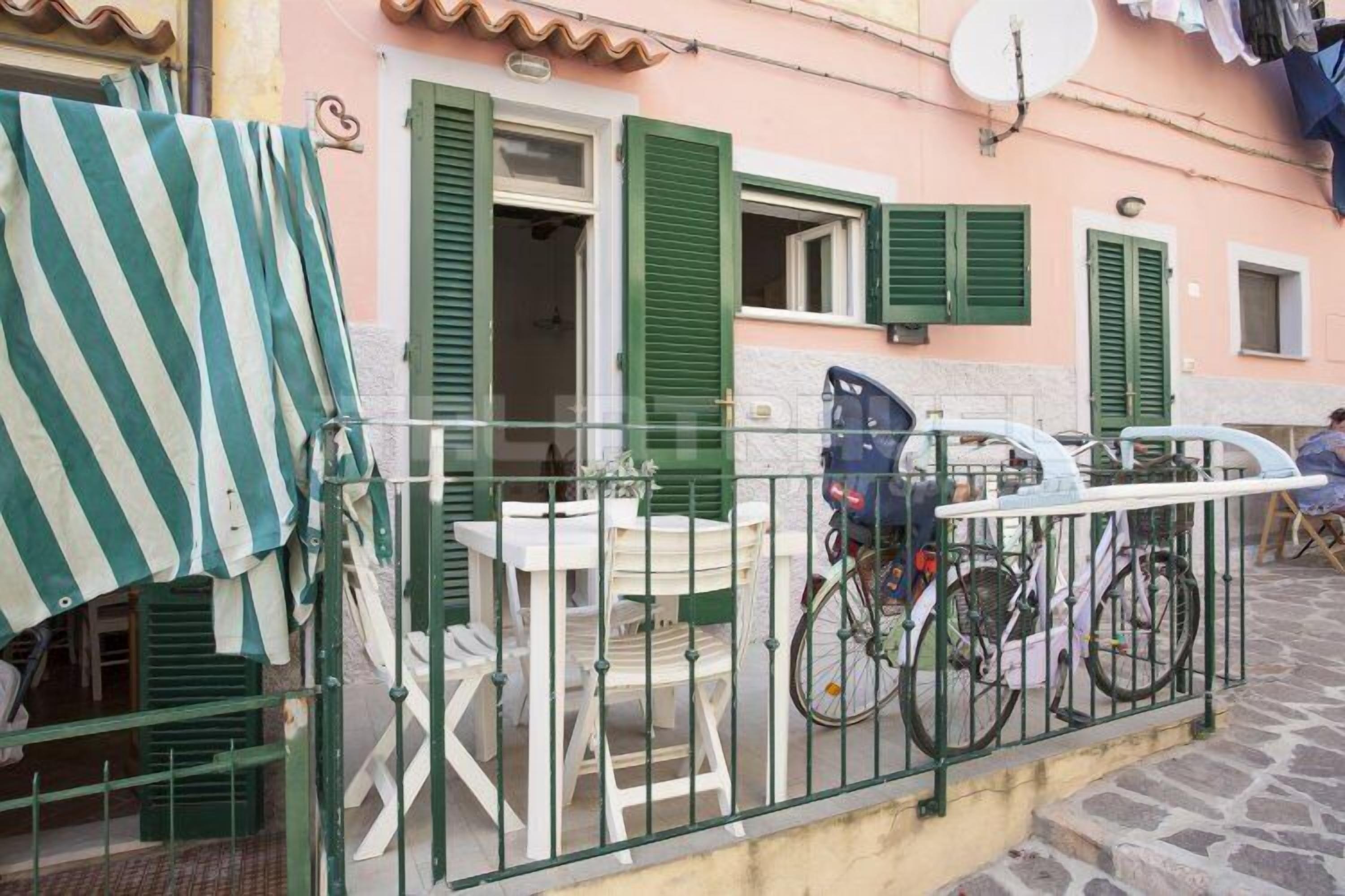 A quaint outdoor seating area with white plastic chairs and tables, green shutters, and a bicycle parked nearby.