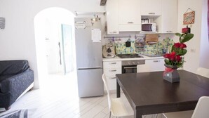 A compact kitchen with white cabinets, a refrigerator, a microwave, and a dining area with a table and chairs.