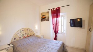 A bedroom with a bed, a nightstand, a TV, and a window with curtains.