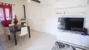 A modern living room with a flat-screen TV, white cabinetry, a dining area with a dark table and white chairs, and a fireplace.