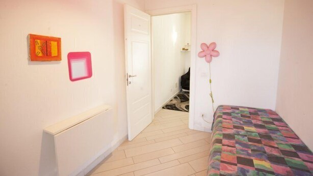 Une chambre à coucher comprenant un lit, un radiateur, une porte donnant sur une autre pièce et un mur orné de deux tableaux encadrés.