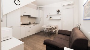 A modern kitchen with white cabinets, a dining table with chairs, and a brown sofa. - Italianway Comfort - Bligny 19 B (Milan)