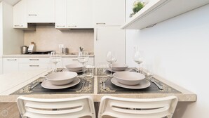 A modern kitchen with white cabinets, a countertop with a coffee machine, and a dining area with a table set for two. - Italianway Comfort - Bligny 19 B (Milan)