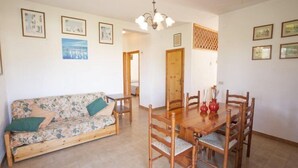 Uma área de refeições com mesa e cadeiras de madeira, um sofá com estofado floral e quadros nas paredes.