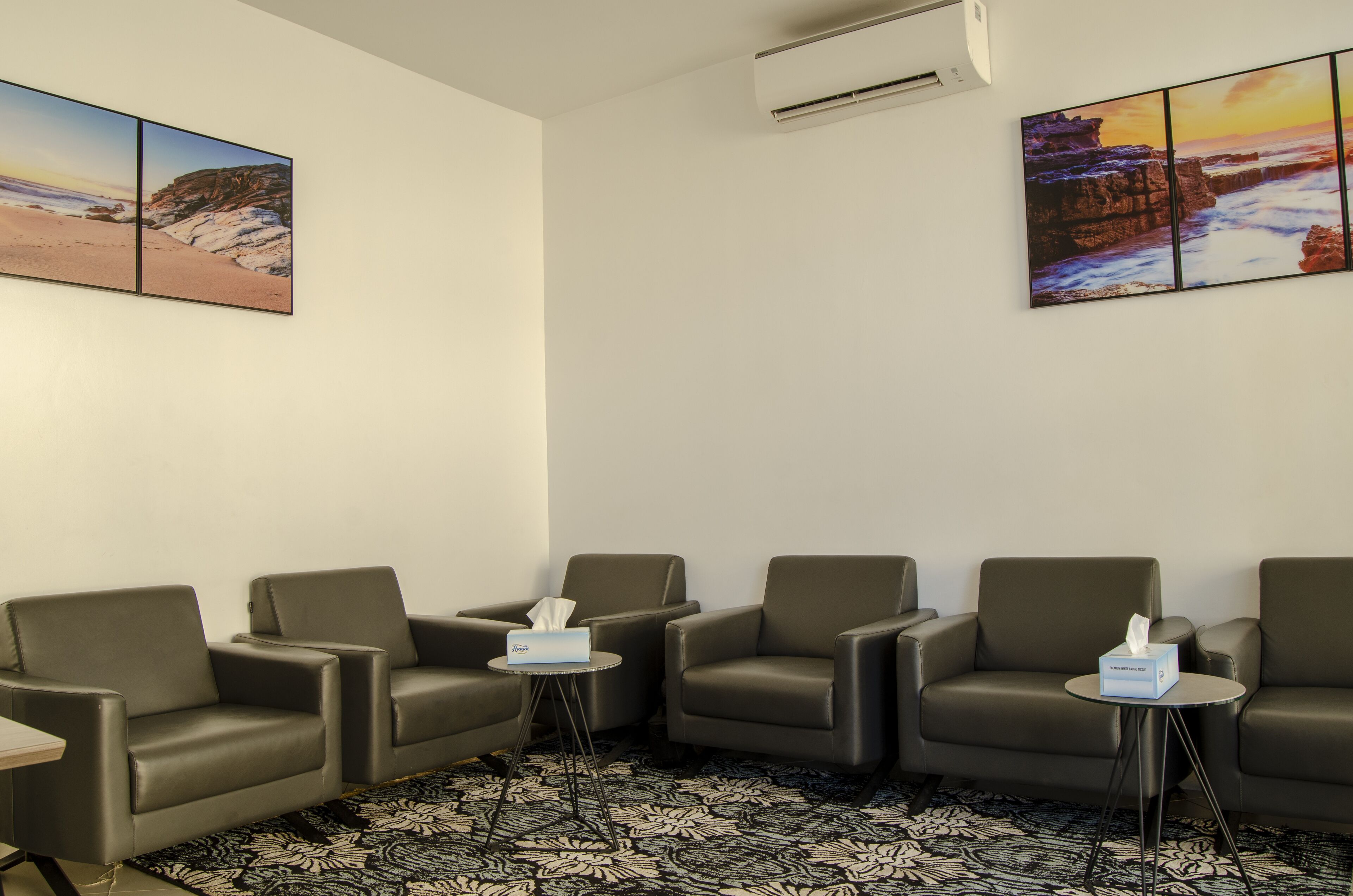 A room with four leather armchairs, a small round table with a tissue box, and two wall-mounted air conditioning units.