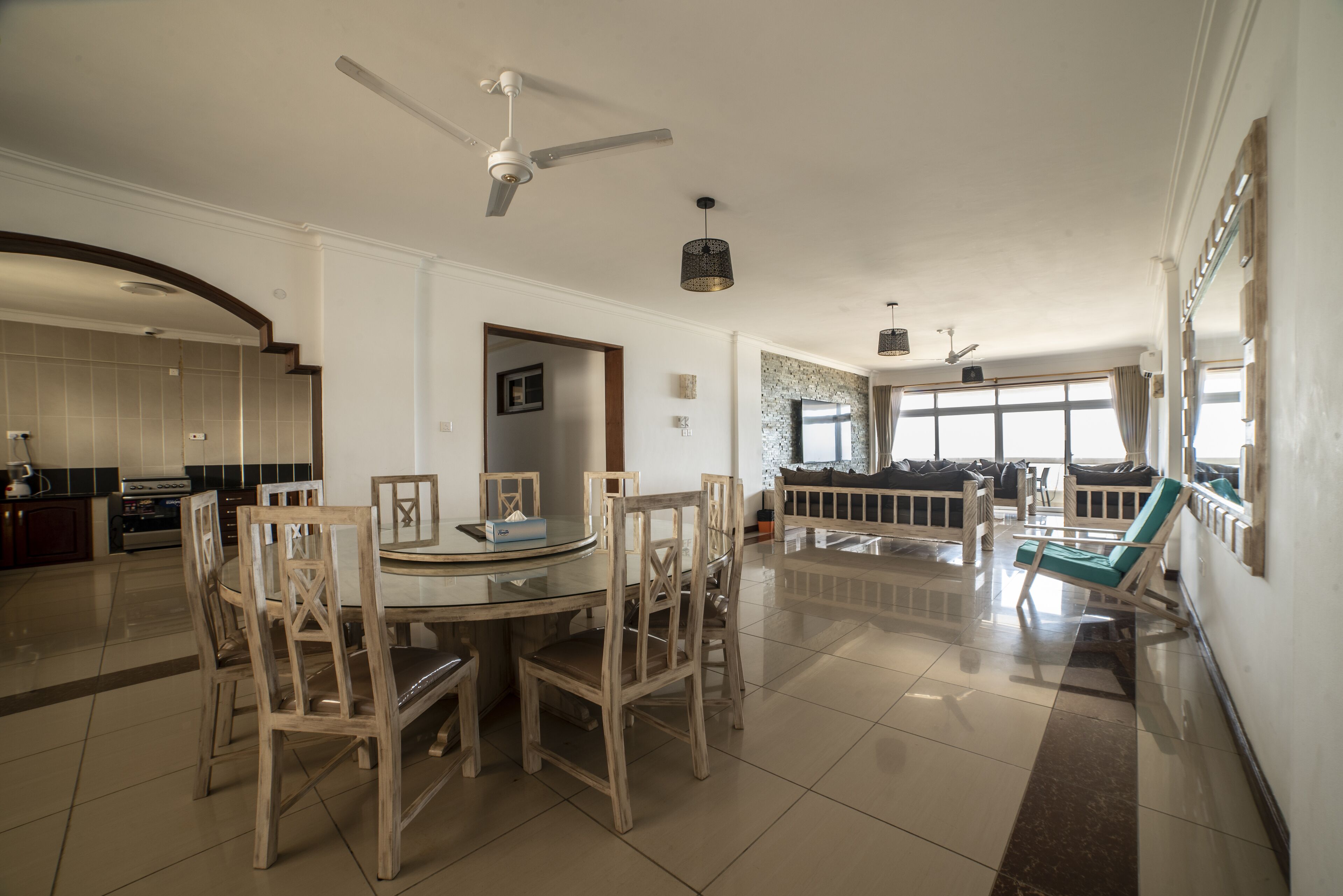 Un'ampia zona giorno con tavolo da pranzo circondato da sedie in legno, una ventola a soffitto e un'ampia finestra che garantisce luce naturale.