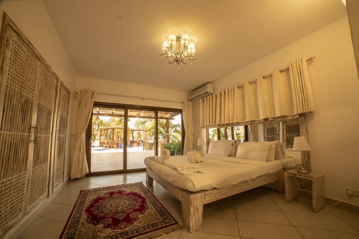 A spacious bedroom with a large bed, a chandelier, a small bedside table, and a view of the outdoors through a sliding glass door.