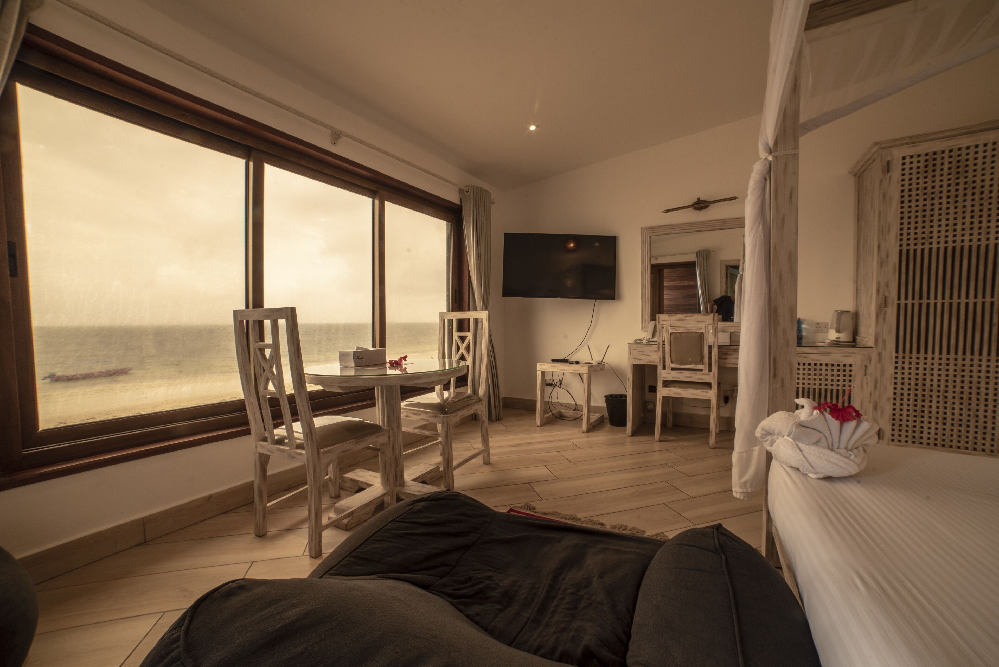 A hotel room with a large window, a bed, a desk, and a television.