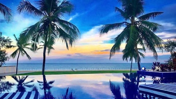 A poolside view with palm trees and a sunset over the ocean.