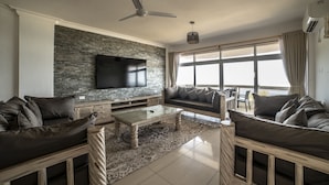 A modern living room with a stone wall, leather sofas, a glass coffee table, and a flat-screen TV.
