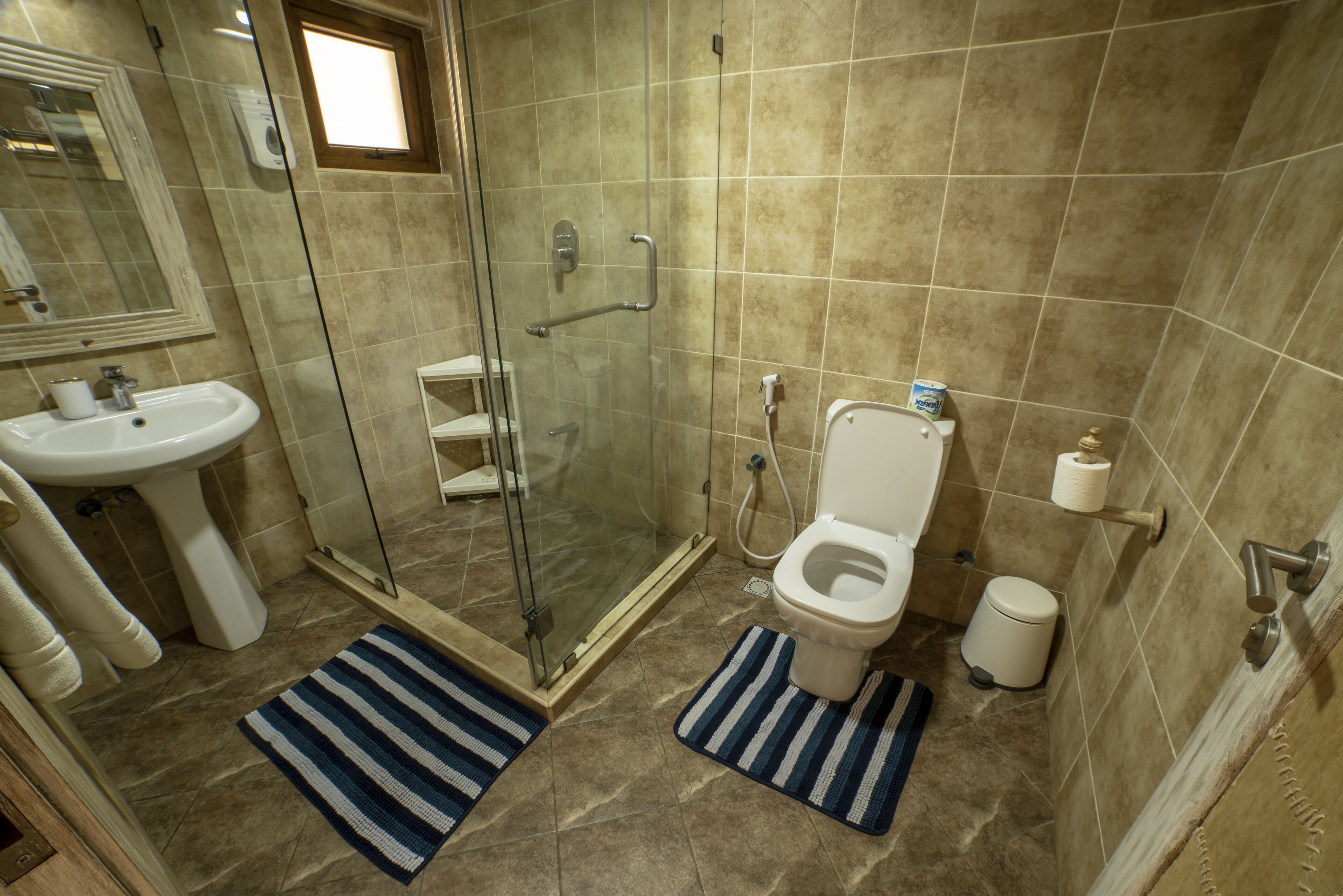 A bathroom with a glass-enclosed shower, a sink, a toilet, and a small window.