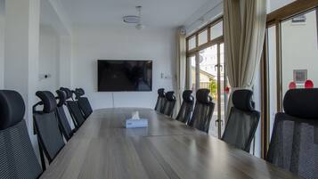 Uma sala de conferências com uma mesa comprida, cadeiras pretas, uma TV de tela plana e uma janela com cortinas.