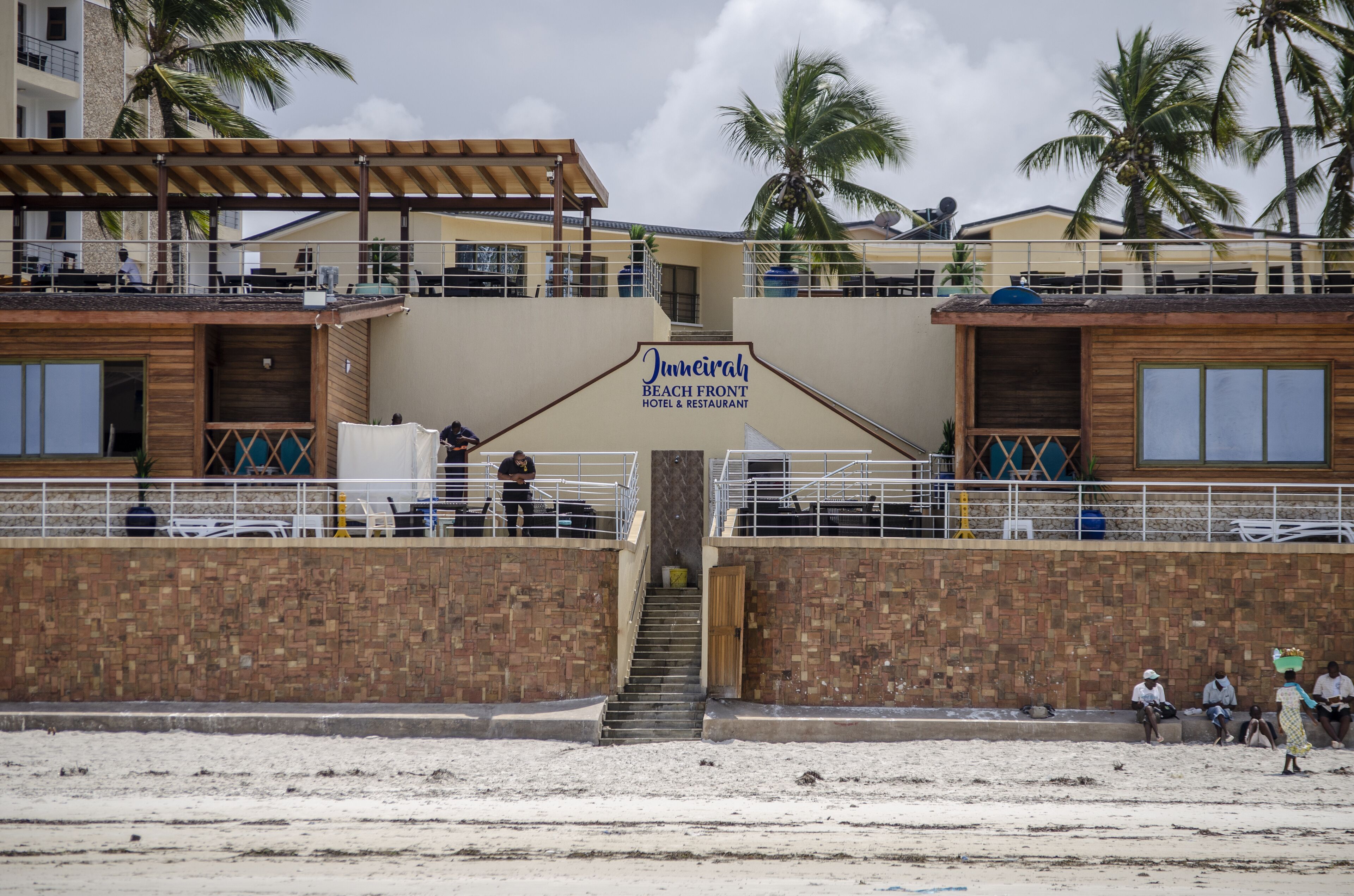 A beachside hotel entrance with a sign reading "Junneirah Beach Front Hotel & Restaurant."
