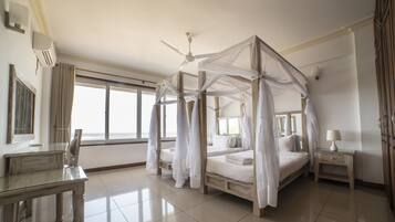 Ein geräumiges Schlafzimmer mit Himmelbett, Deckenventilator und großem Fenster mit Blick auf den Strand.