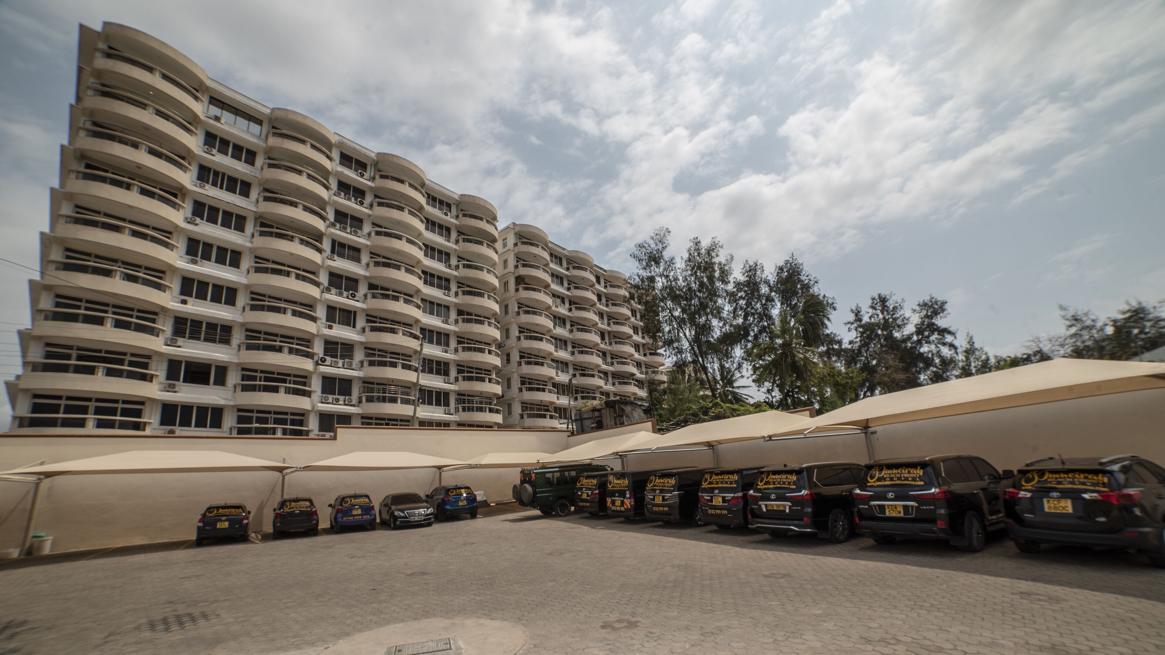 A parking area with several vehicles and a large building with multiple balconies.