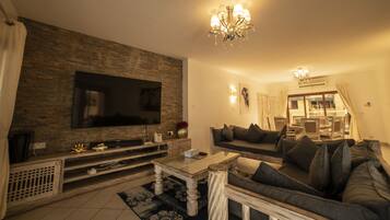 A living room with a flat-screen TV mounted on a stone wall, a sofa, a coffee table, and a chandelier.