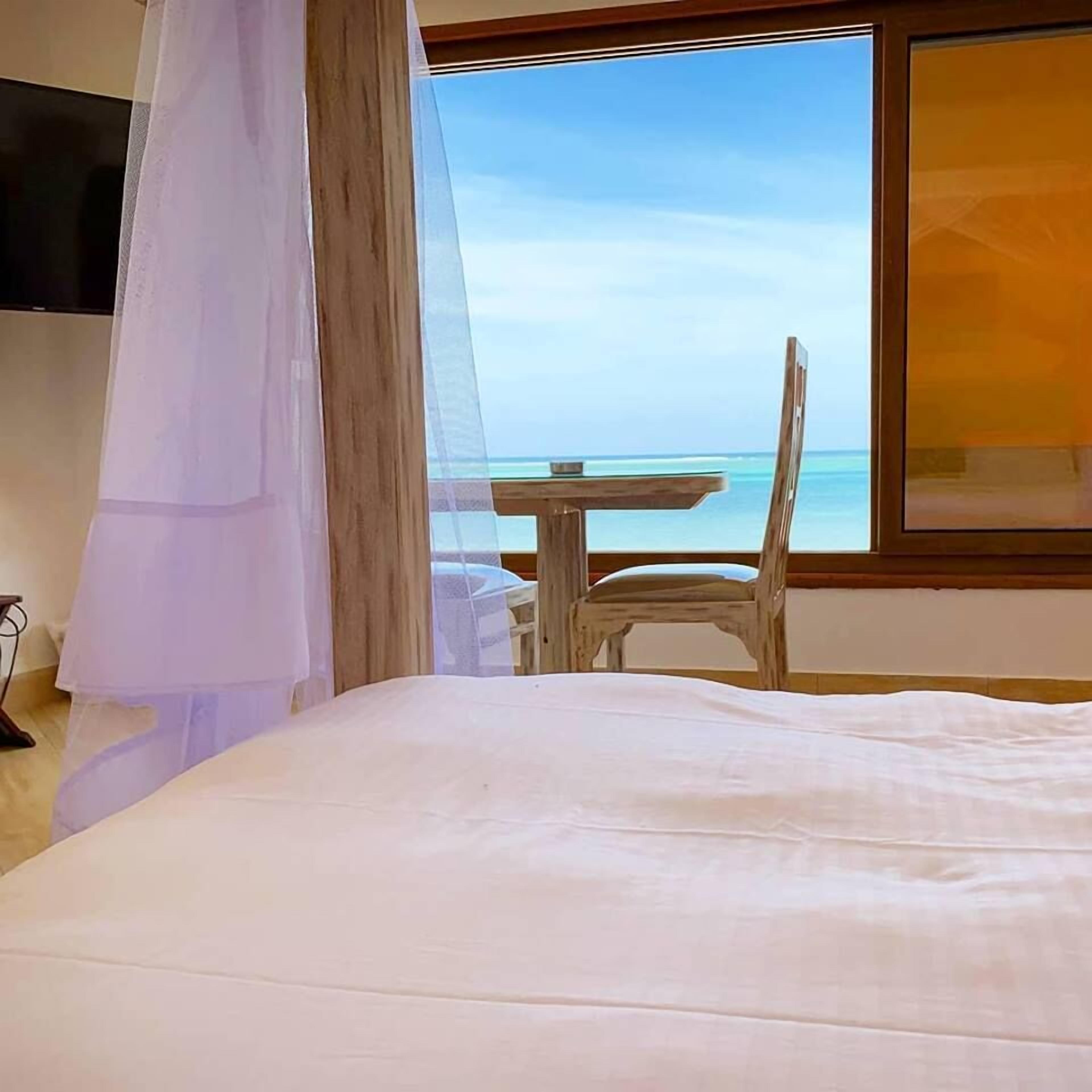 Ein Schlafzimmer mit einem Bett, einem Sessel, einem Tisch und Blick auf den Ozean.