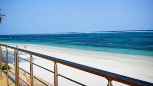 A beach with a metal railing, clear blue water, and a distant lighthouse.
