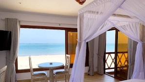 A room with a bed, a table with chairs, a TV, and a view of the sea.