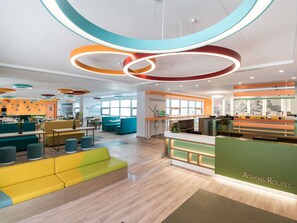 A modern interior with a reception desk, seating areas, and a kitchen in the background. - ibis Styles Athens Routes (Athens)