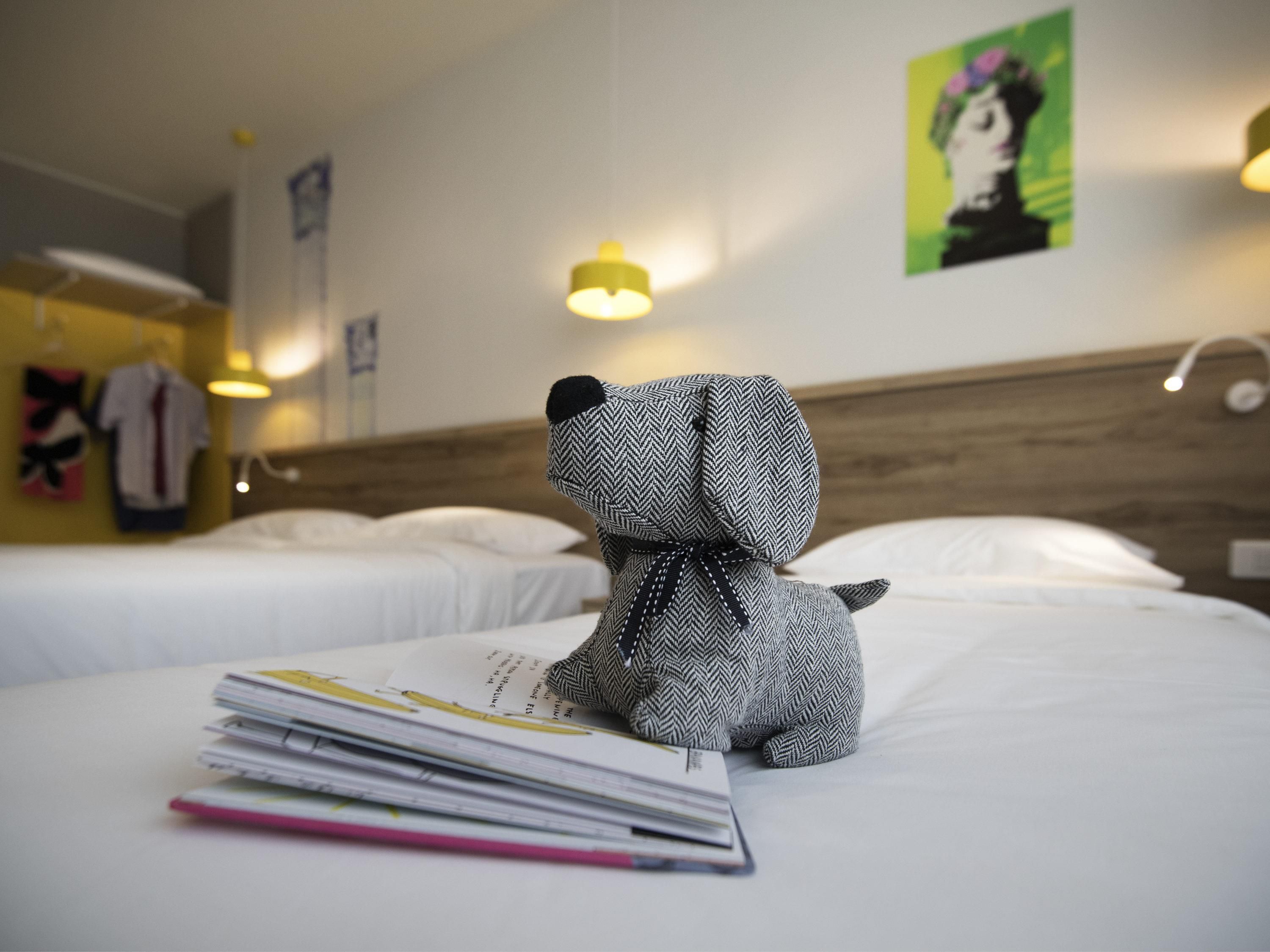 Una habitación de hotel con una cama, un peluche y una revista.