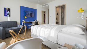 A modern hotel room with a bed, a desk, a sofa, and a TV on the wall. - ibis Styles Athens Routes (Athens)