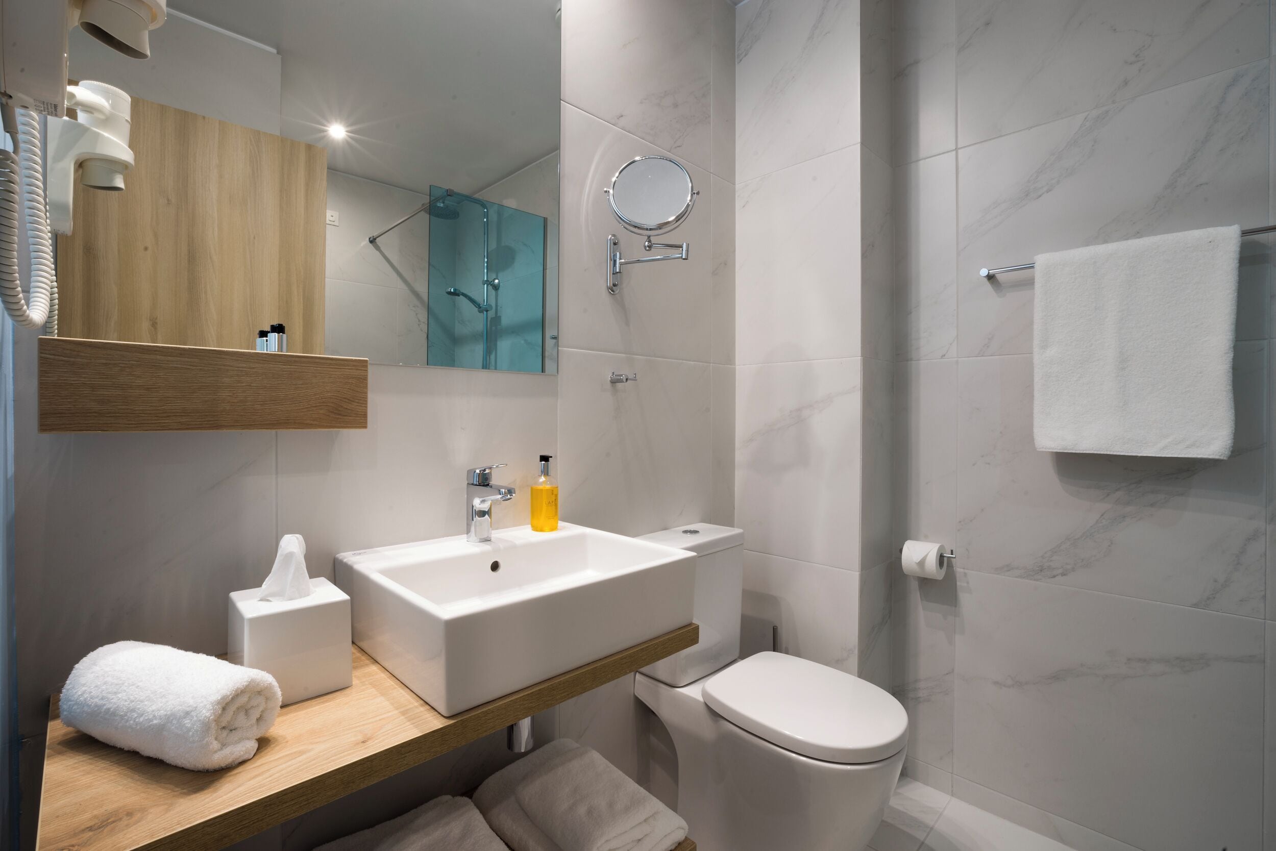 A modern bathroom with a wooden vanity, a white sink, a toilet, and a glass shower enclosure.