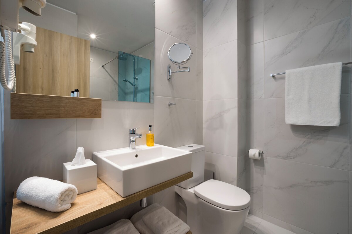 A modern bathroom with a wooden vanity, a white sink, a toilet, and a glass shower enclosure.