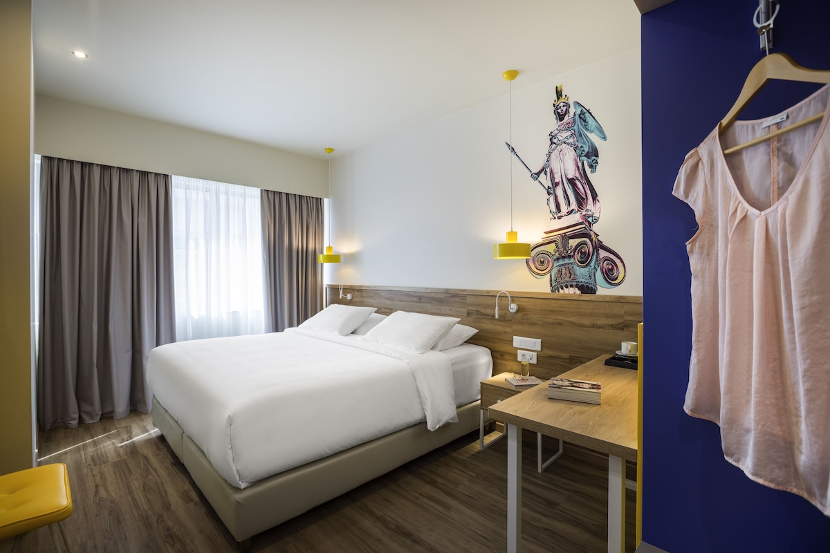 A hotel room with a large bed, a wooden headboard, a desk, and a wall-mounted artwork.