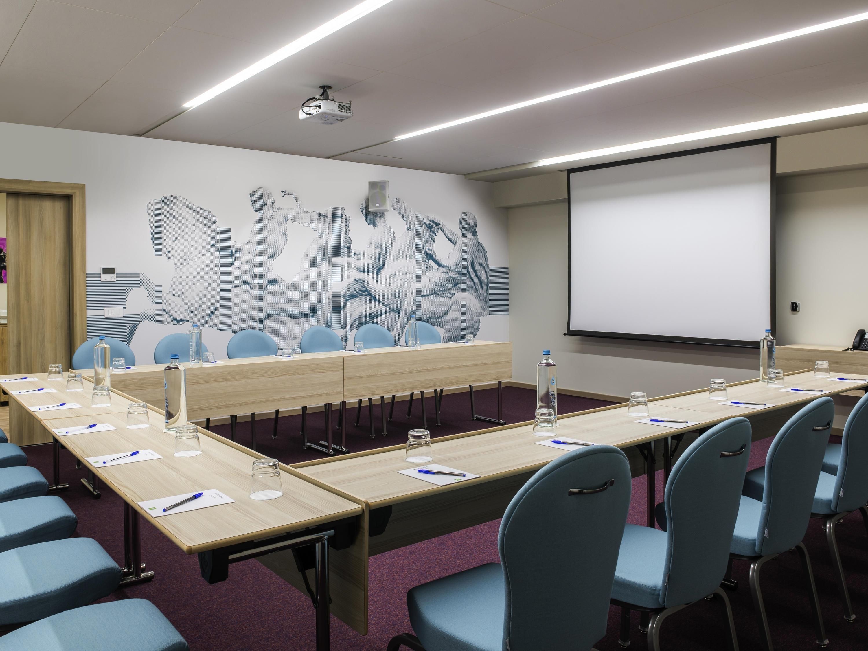 Une salle de conférence avec une longue table, des chaises, un écran de projection et une grande fresque abstraite sur le mur.