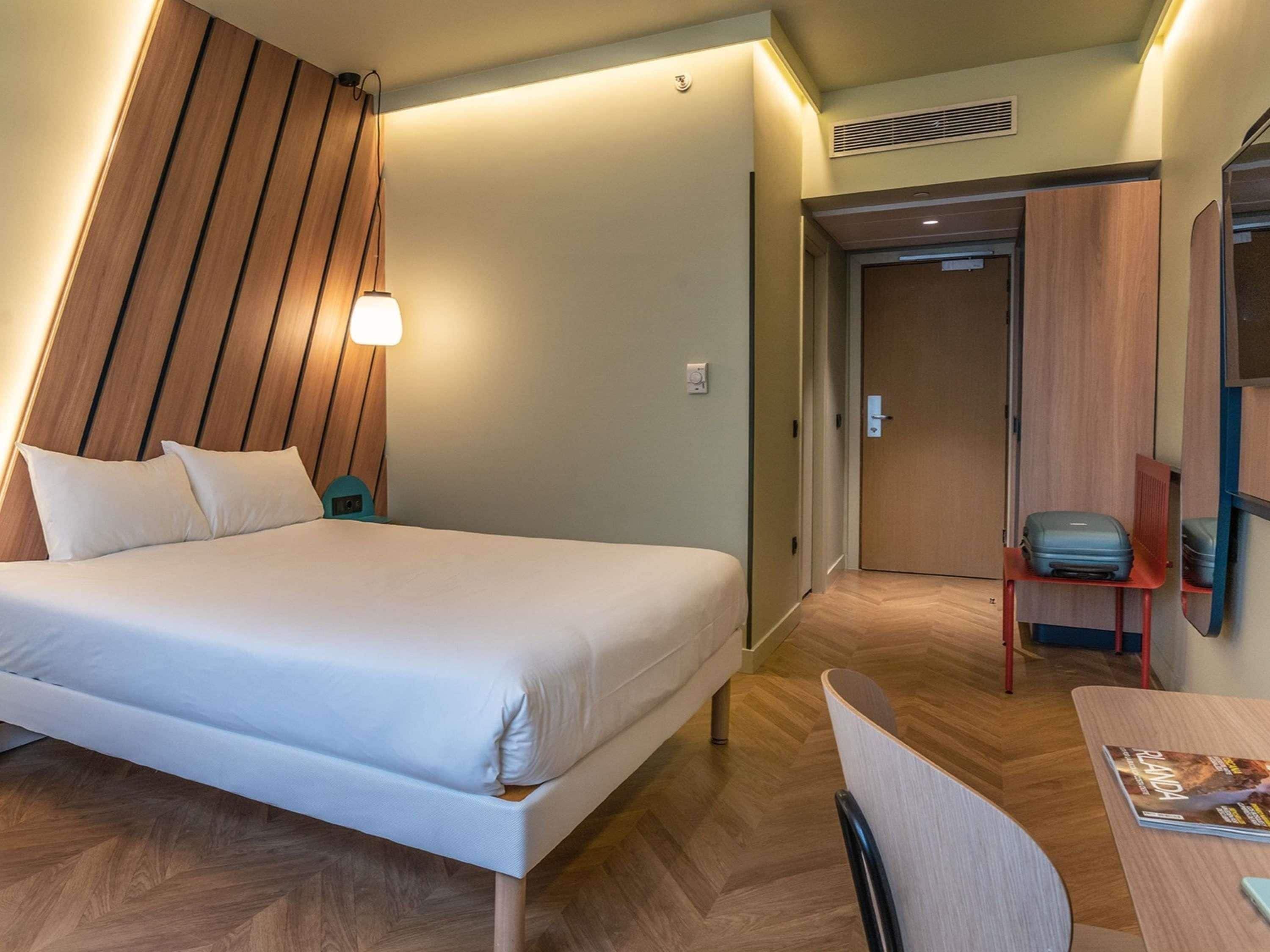 A hotel room with a bed, a desk, a chair, and a door.