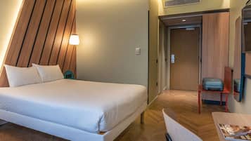Una habitación de hotel con una cama, un escritorio, una silla y una puerta.