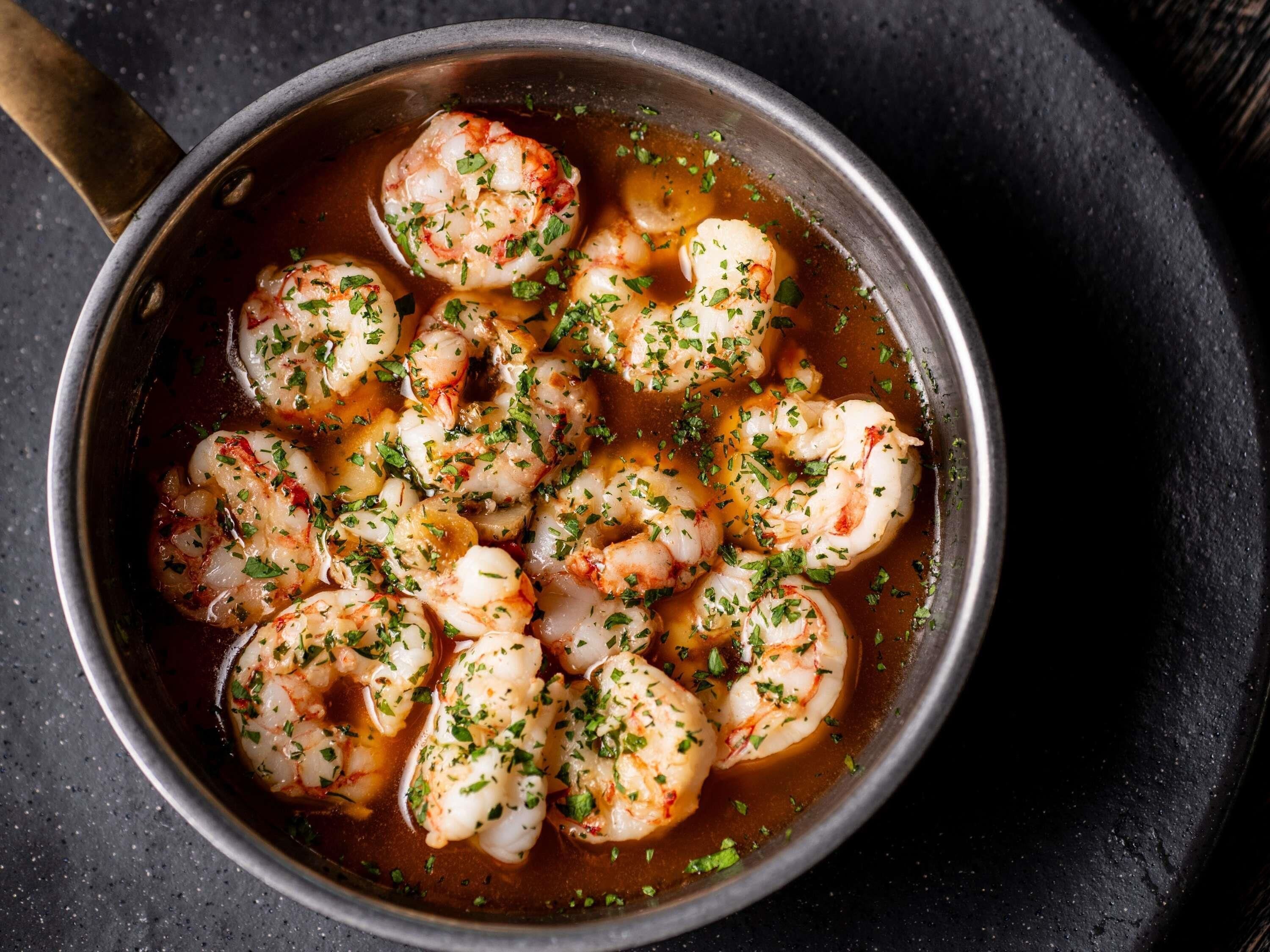 A pan of shrimp cooked in a sauce, garnished with herbs.