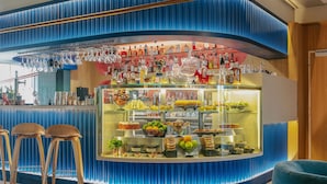 A bar area with stools, a glass display case with food items, and a variety of bottles.