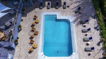 Vista aèria d'una zona de piscina al terrat, amb diverses gandules i taules disposades al seu voltant.