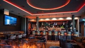 A bar area with seating, a television screen, and a bar stocked with bottles. - Qube Hotel Bahnstadt (Heidelberg)
