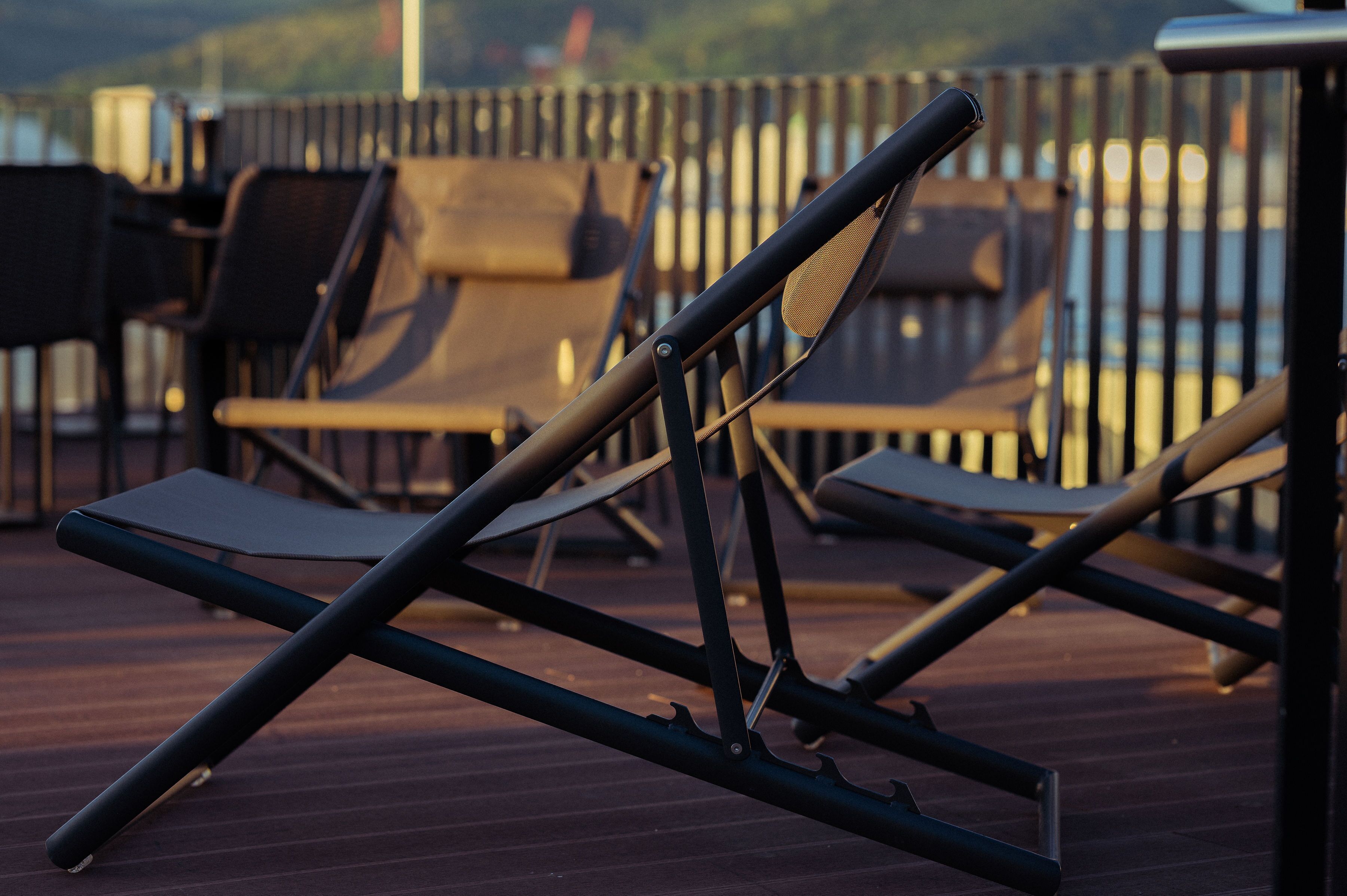Eine Terrasse mit Liegestühlen und einem Tisch, mit Blick auf ein Gewässer.