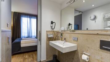 A modern hotel room with a bed, a bathroom with a sink, mirror, and towel rack.
