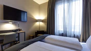 A hotel room with a bed, a desk with a chair, a TV mounted on the wall, and a lamp.