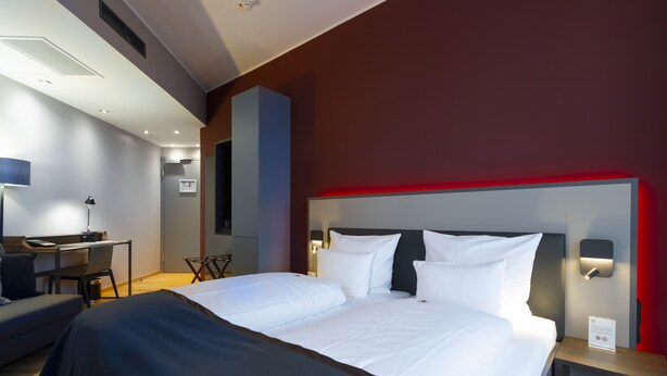 A modern hotel room with a large bed, bedside tables, a desk, and a chair. - Qube Hotel Bahnstadt (Heidelberg)