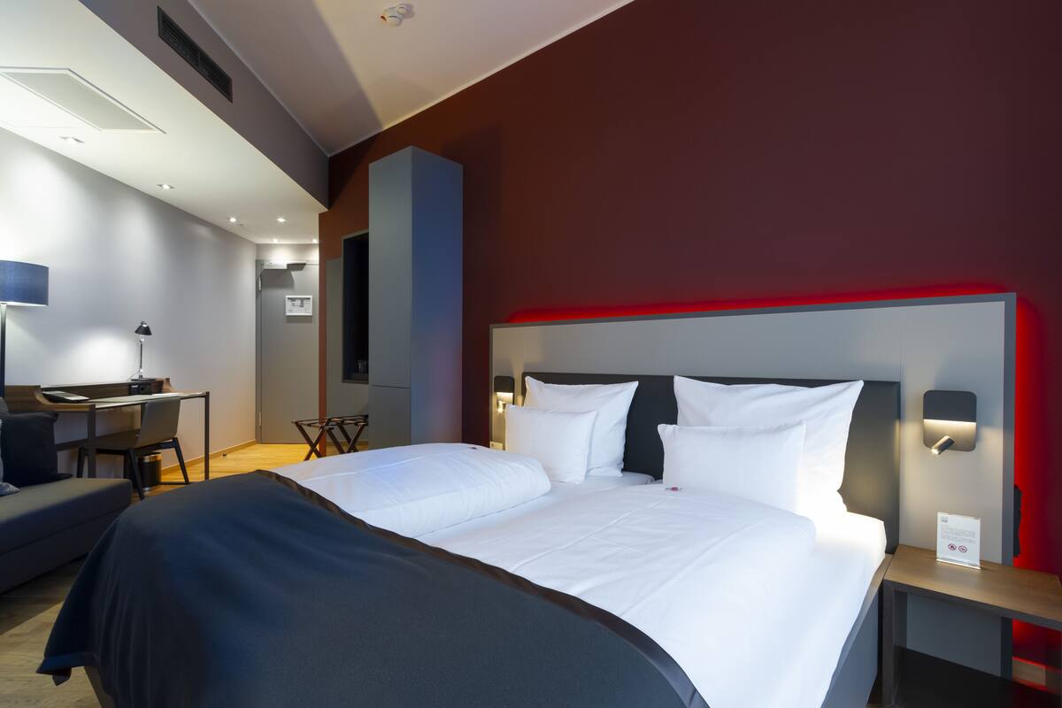 A modern hotel room with a large bed, bedside tables, a desk, and a chair.