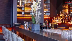 A bar area with high stools, a bar counter, and hanging pendant lights. - Qube Hotel Bahnstadt (Heidelberg)