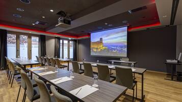Un salón de conferencias con una larga mesa, sillas, una pantalla de proyector y un ventanal grande.