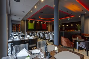 L’intérieur d’un restaurant présente de nombreuses tables et chaises, un bar et un plafond au design moderne agrémenté d’un éclairage encastré.