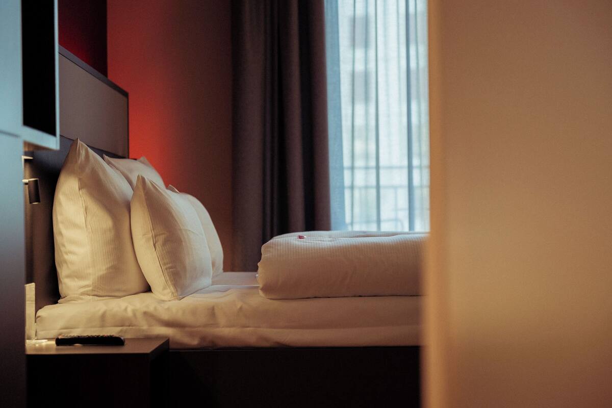 A neatly made bed with pillows and a remote control on a bedside table in a hotel room.