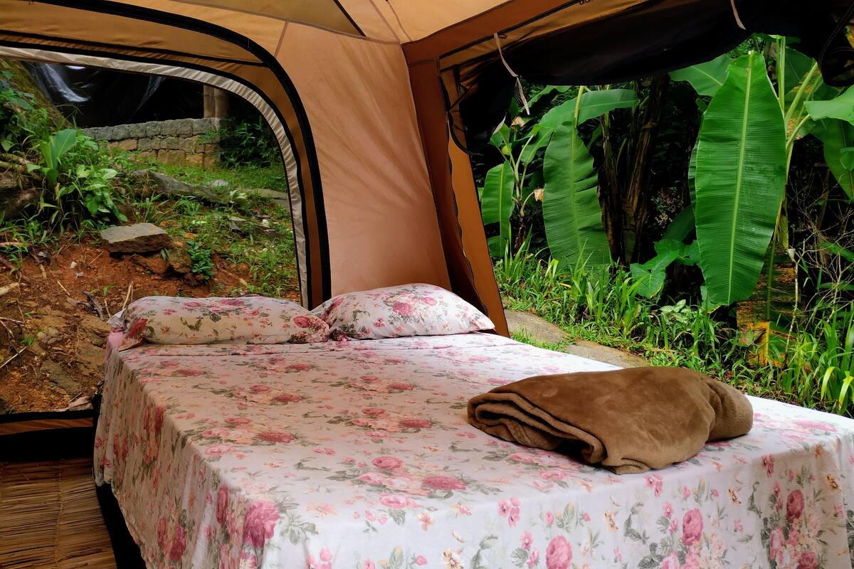 A tented room with a bed, floral bedding, and a view of lush greenery outside.