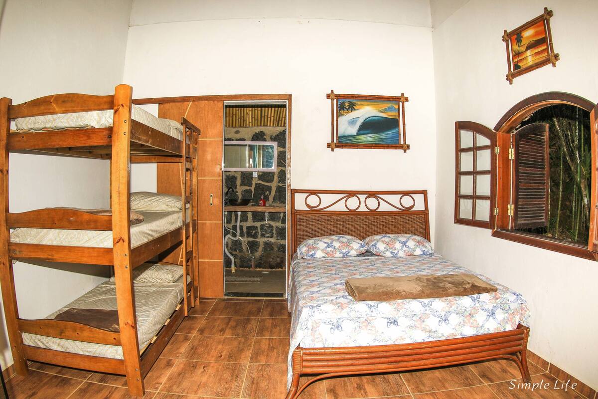 A room with a bunk bed, a single bed, a window with shutters, and a painting on the wall.