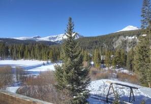 A snowy mountain landscape with a clear sky, a wooden bench, and a forested area.