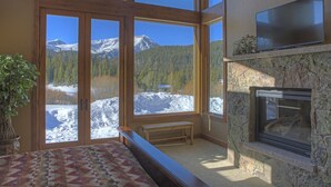 Ein Zimmer mit großen Fenstern und Blick auf die Berge, mit Kamin aus Stein und einer Bank.